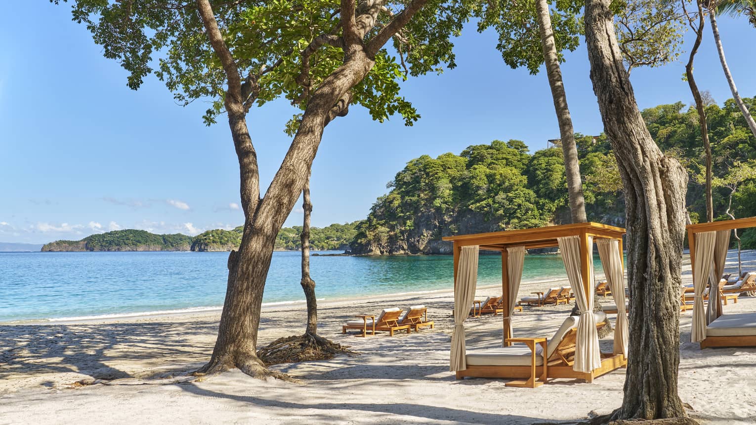 Cabanas and lounge chairs arranged on the beach; blue skies and mountain views