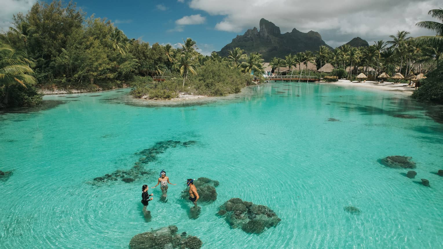 Aerial view of three guests standing in the clear turquoise water of the lagoon at the Dive Centre