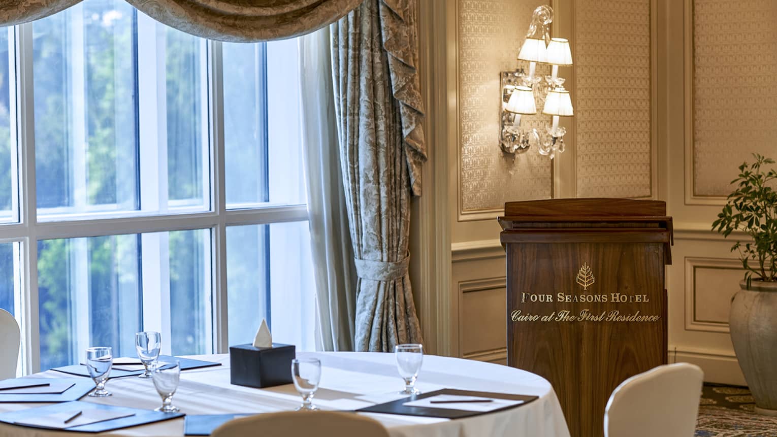 Round table by sunny window, speaker podium with Four Seasons Hotel Cairo at the First Residence logo