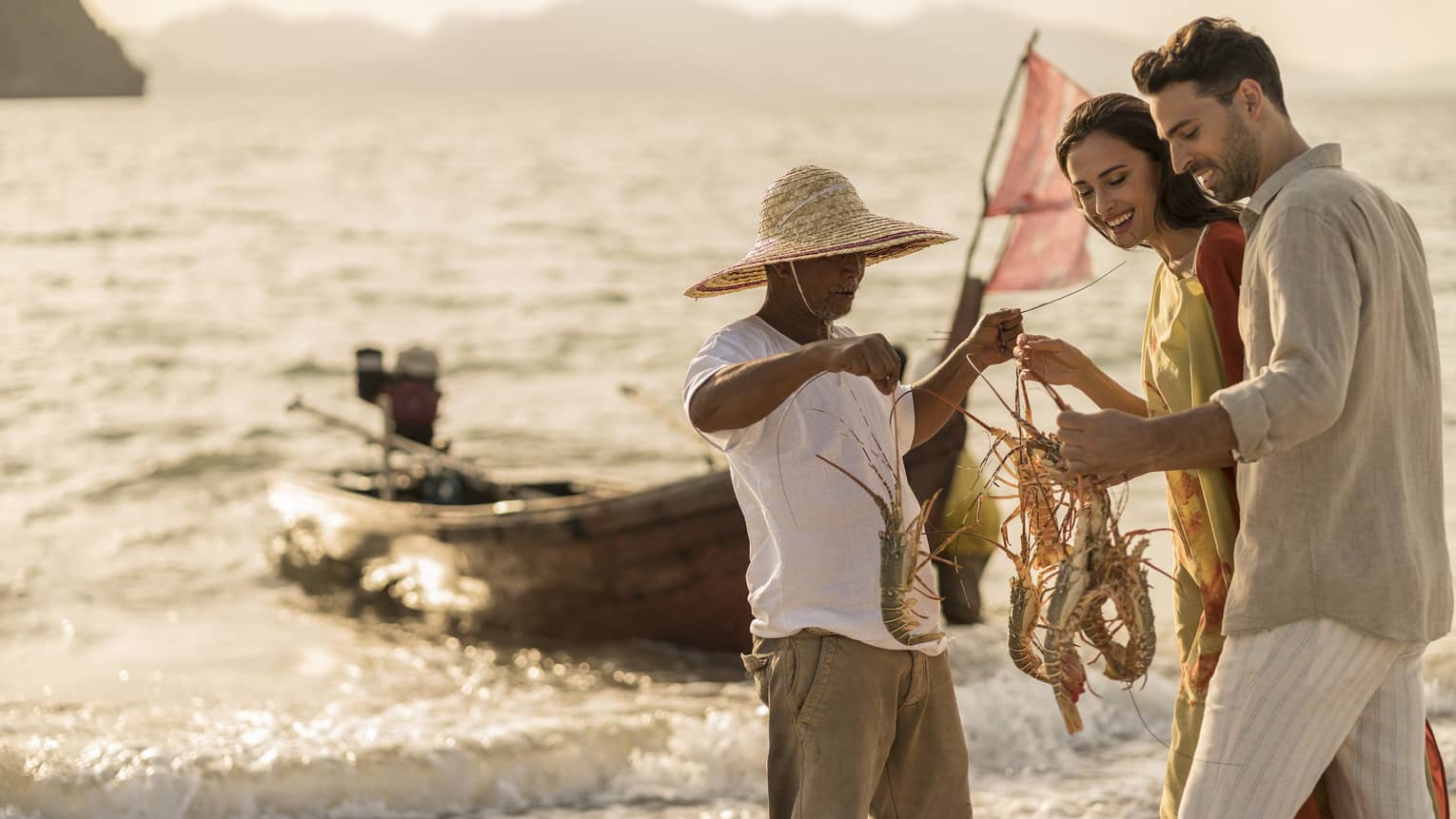 A four seaons fishing guide is holding and showing 4 lobsters to a man and a woman