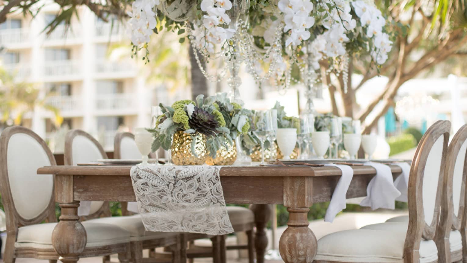 Crystal chandelier, white flowers hang over outdoor garden dining table