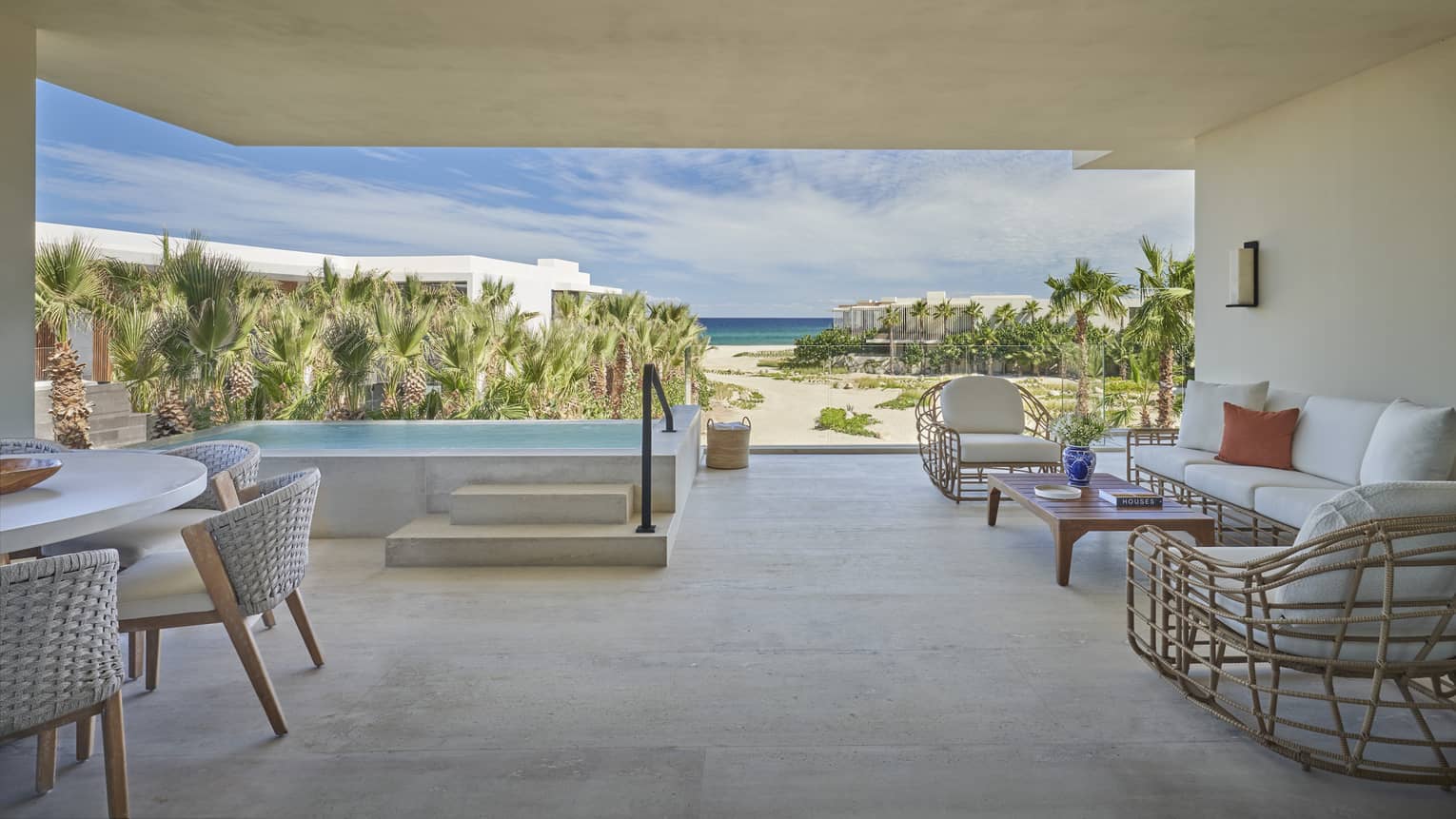 Modern terrace with white seating vignette, dining table, steps up to private pool, and beachfront view