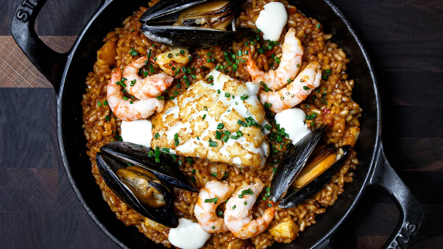 Prawns, squid and mussels on a bed of red Bomba rice in a black Staub brand cast iron skillet 