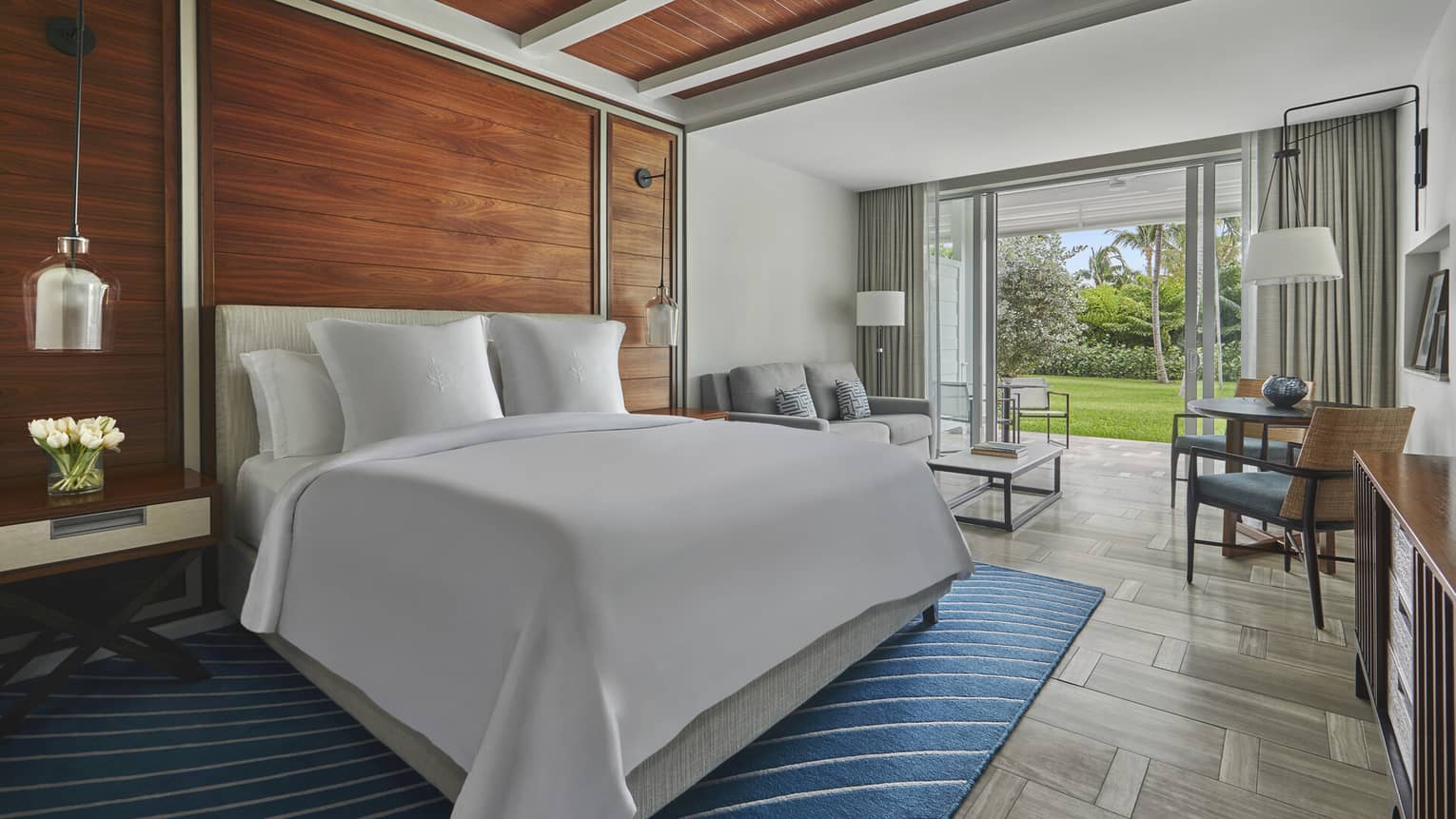 Room with a king-size bed, wooden accent wall and large glass doors opening to a green garden patio area at a Four Seasons luxury resort