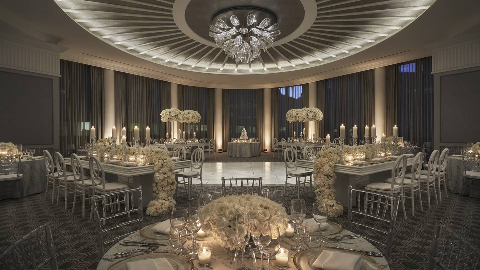 The Four Seasons Boston One Dalton Beacon Ballroom is decorated with formal white floral tables with lit candles. 