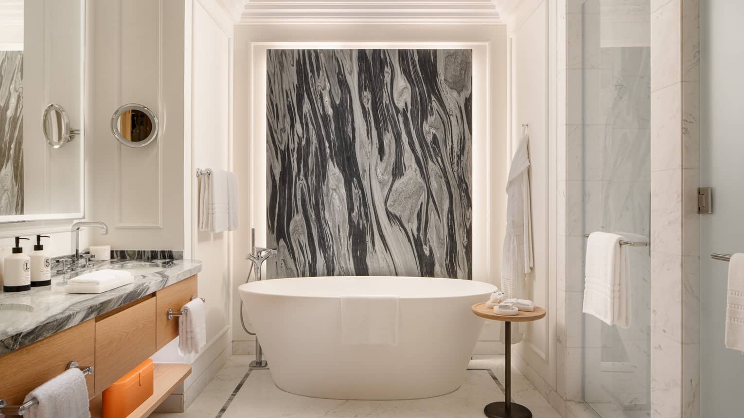 Elegant bathroom with a freestanding tub, black and white marble accent wall, glass shower and vanity with marble countertop.