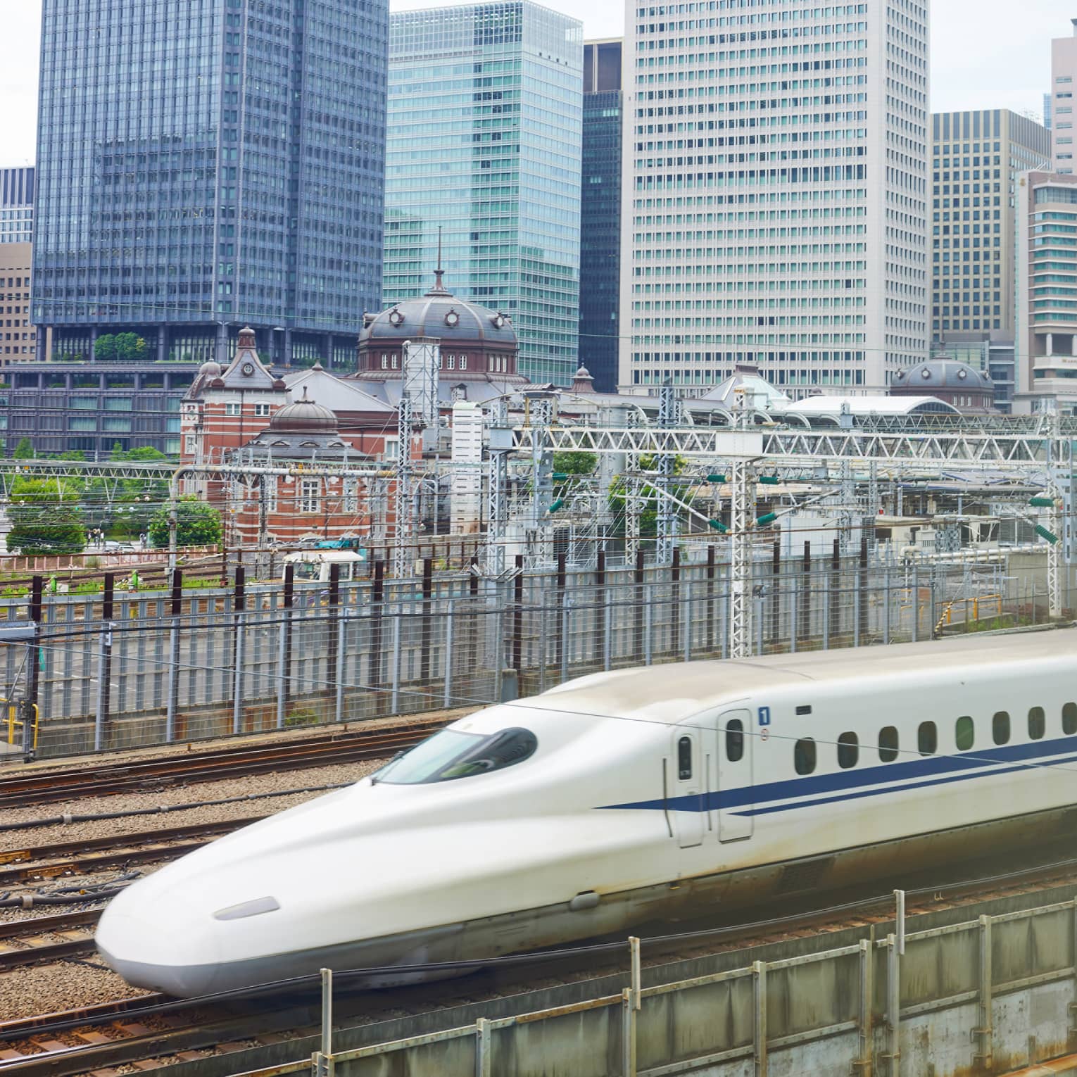 The Shinkansen bullet train speeds past Tokyo's railway station dwarfed by the skyline of rectangular, glass high-rises.