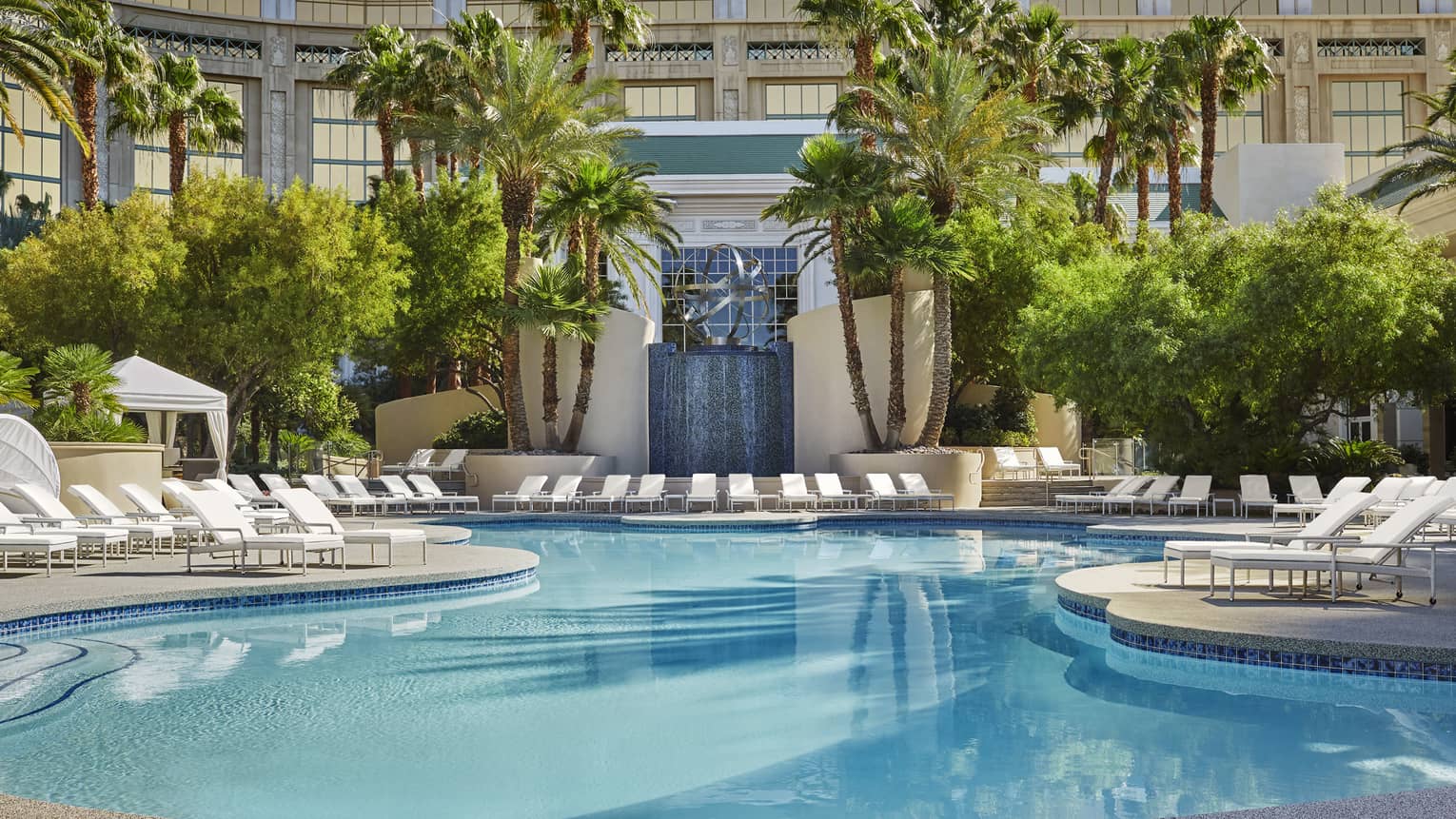 Outdoor hotel pool surrounded by white lounge chairs and palm trees