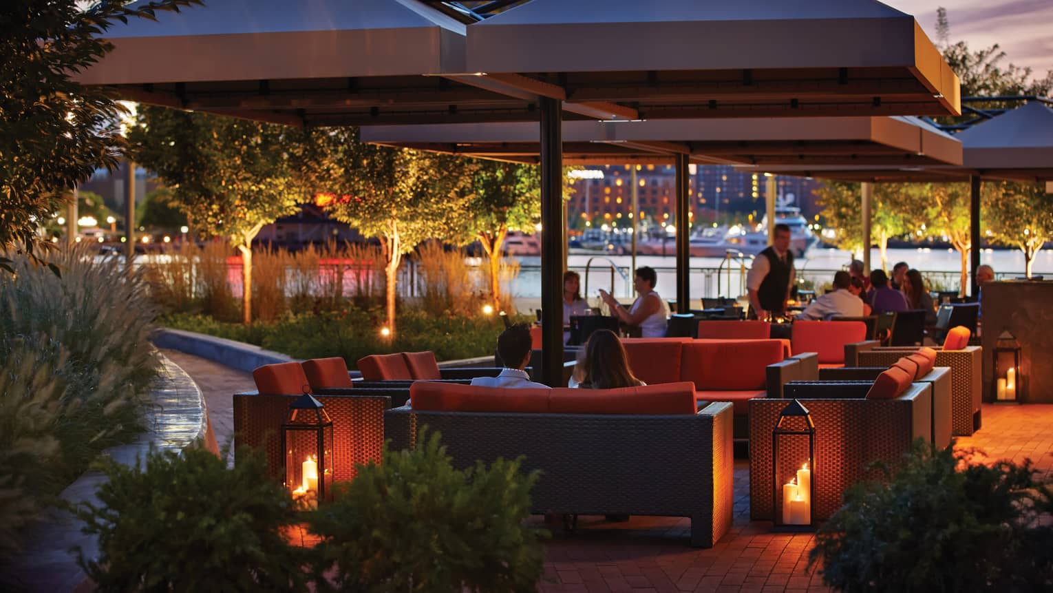 Guests lounge on red patio sofas, chairs under umbrellas