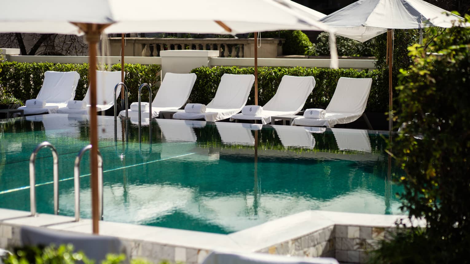 Outdoor pool lined by a row of white lounge chairs and umbrellas