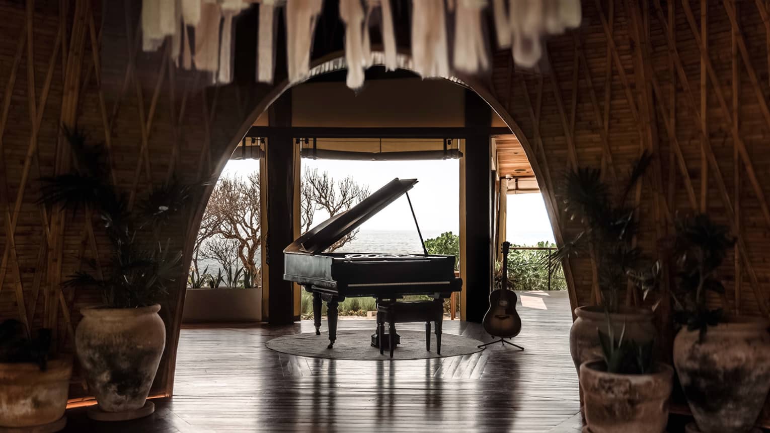 Black grand piano sits in the centre of a room that opens up to the ocean in the distance