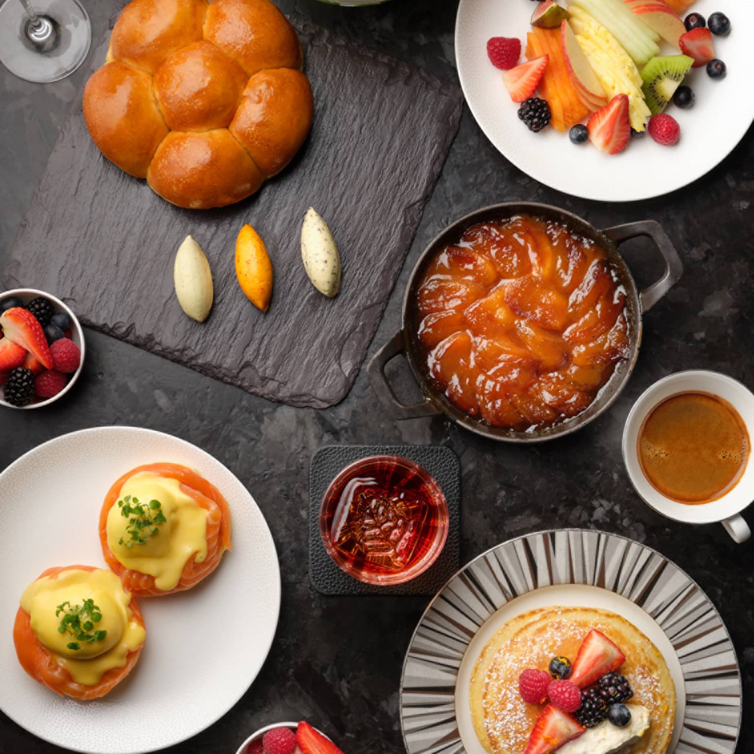 Brunch plates with pastries, fruits, pancakes and coffees on black table