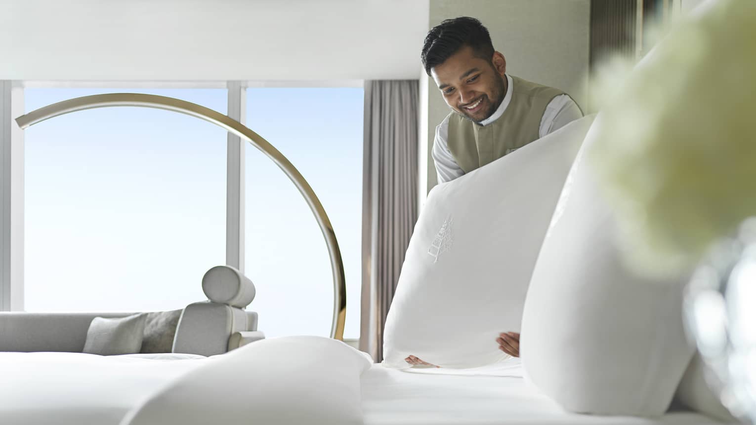 Smiling Four Seasons team member is fluffing the pillow on a freshly made made