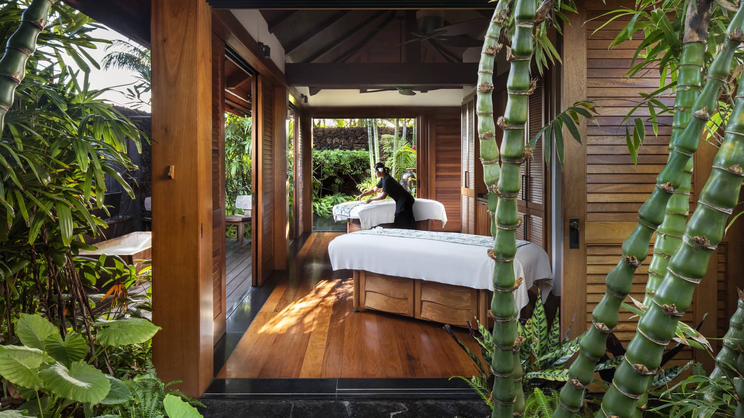 Spa staff spreads sheet on couples massage beds on open-air pavilion