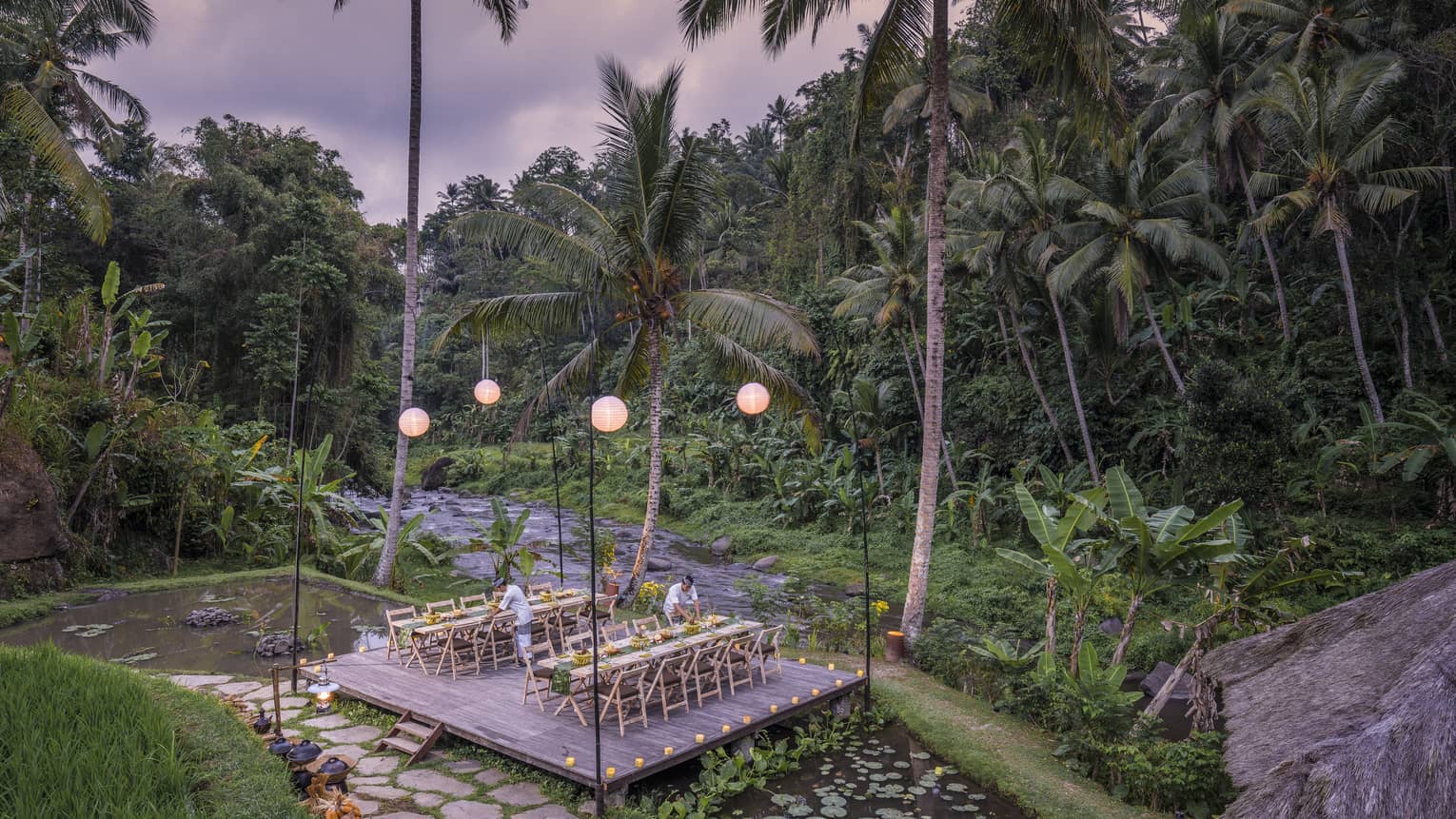 Megibung Dinner is set on a wooden deck as the sun sets beyond lush trees