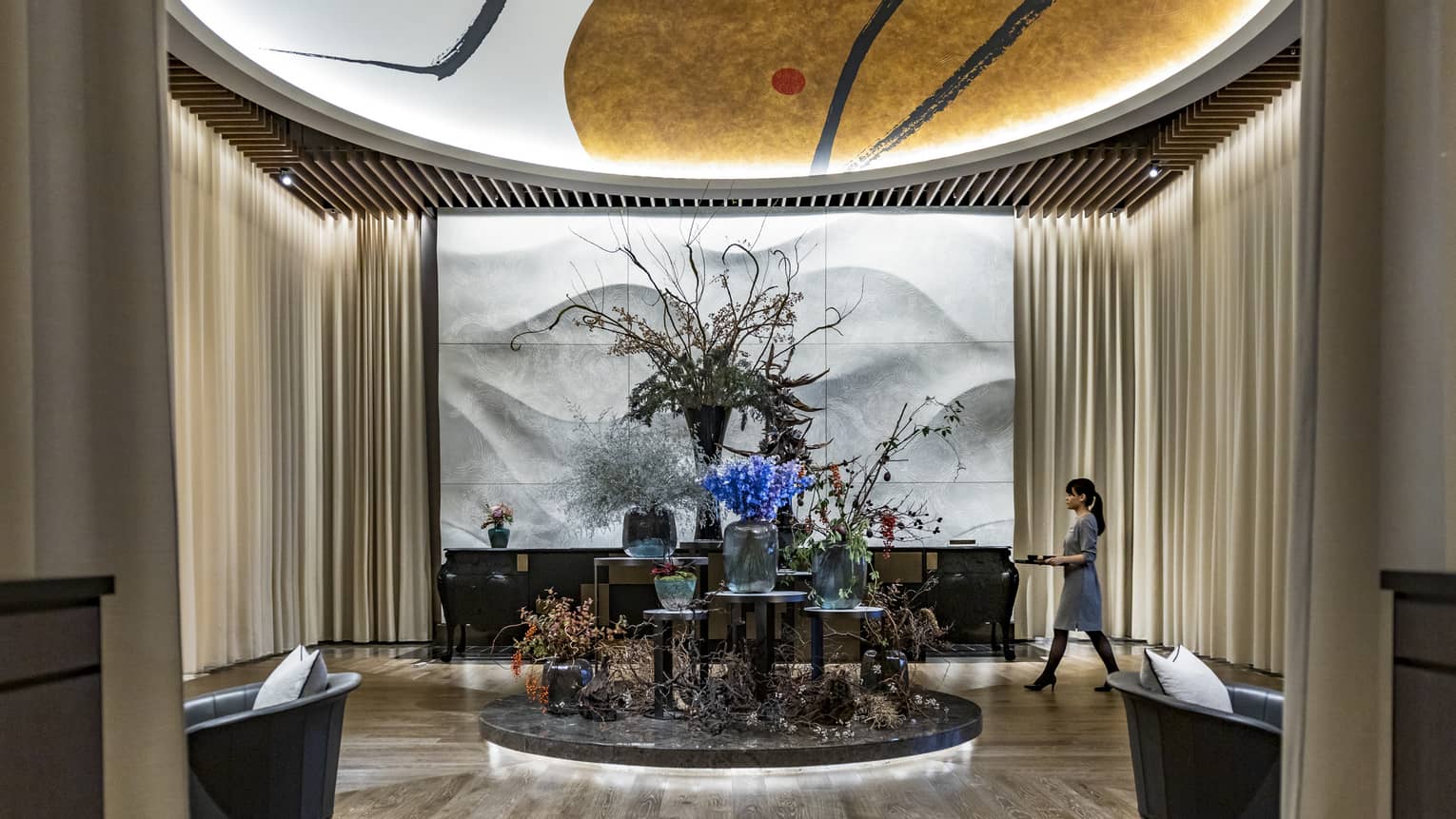 Four Seasons hotel lobby with floral arrangements on a central display and a staff member walking nearby
