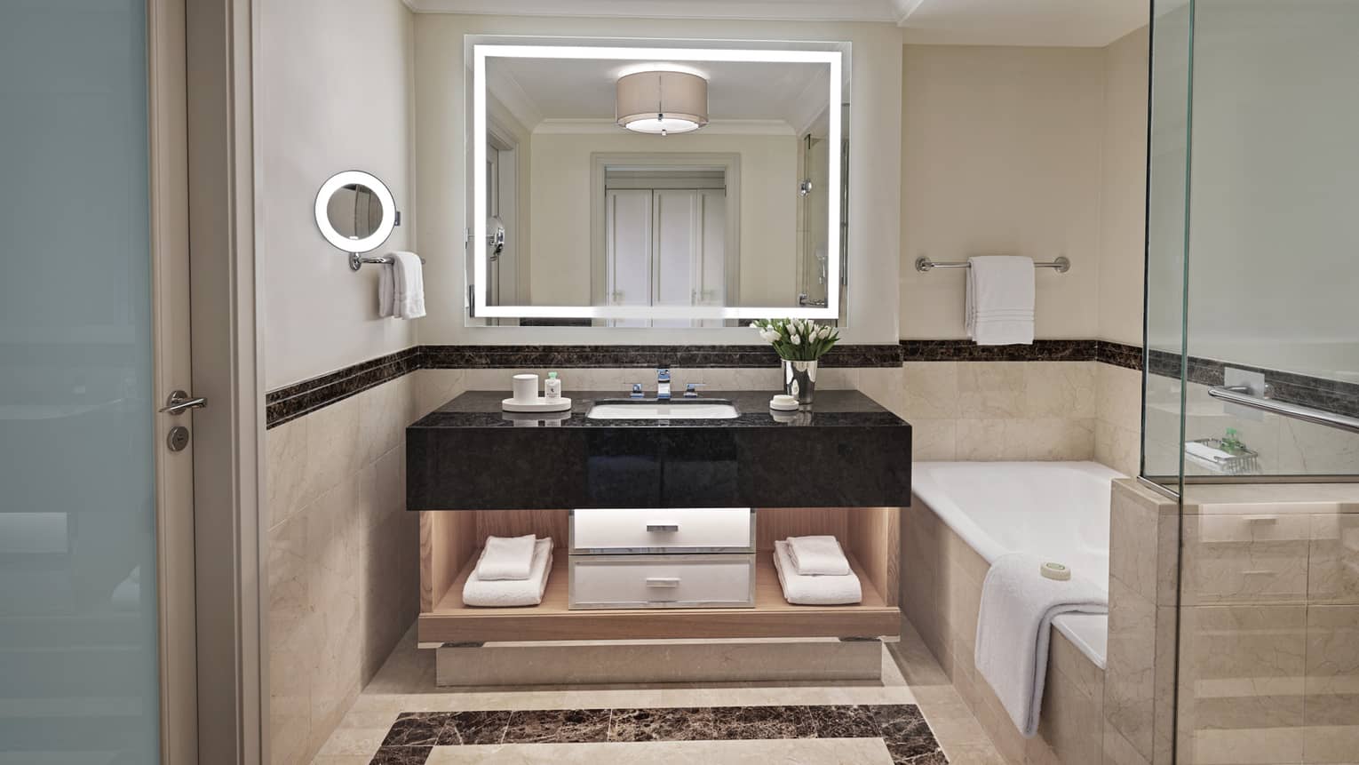 Bathroom with lighted mirror, black marble vanity, tub and separate glass shower