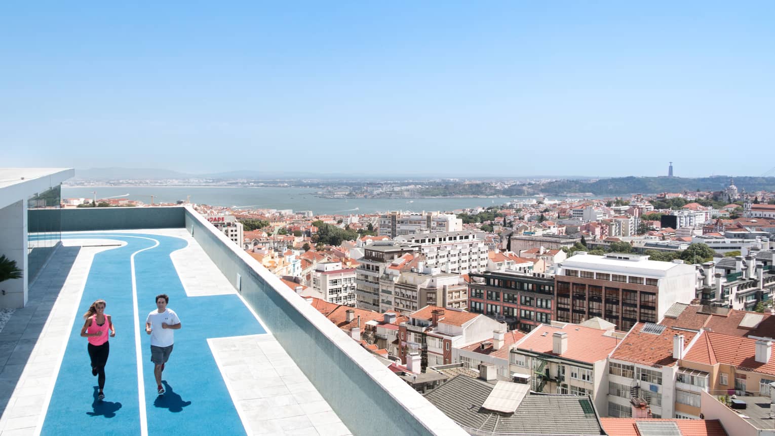 Two people run on blue, rooftop running track, overlooking Lisbon