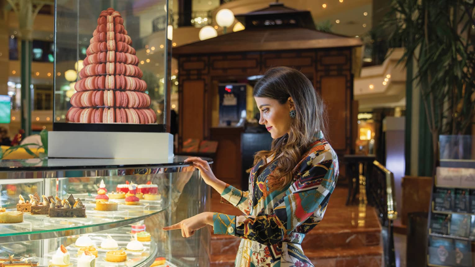 A woman points to a pastry within a glass container of sweets at La Gourmandise