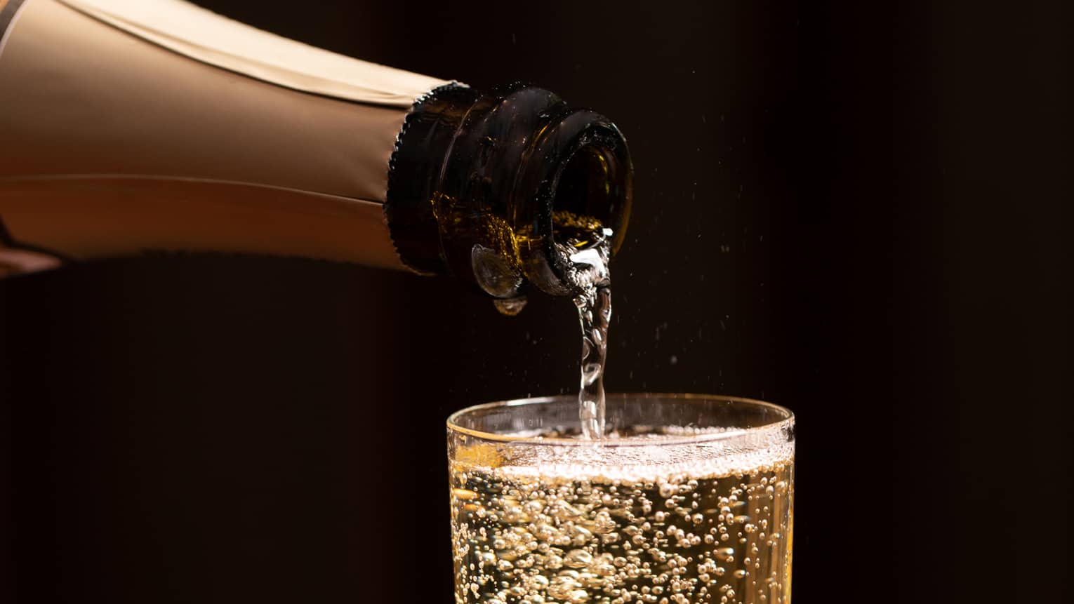 A bottle of champagne is poured into a glass as bubbles float to the top