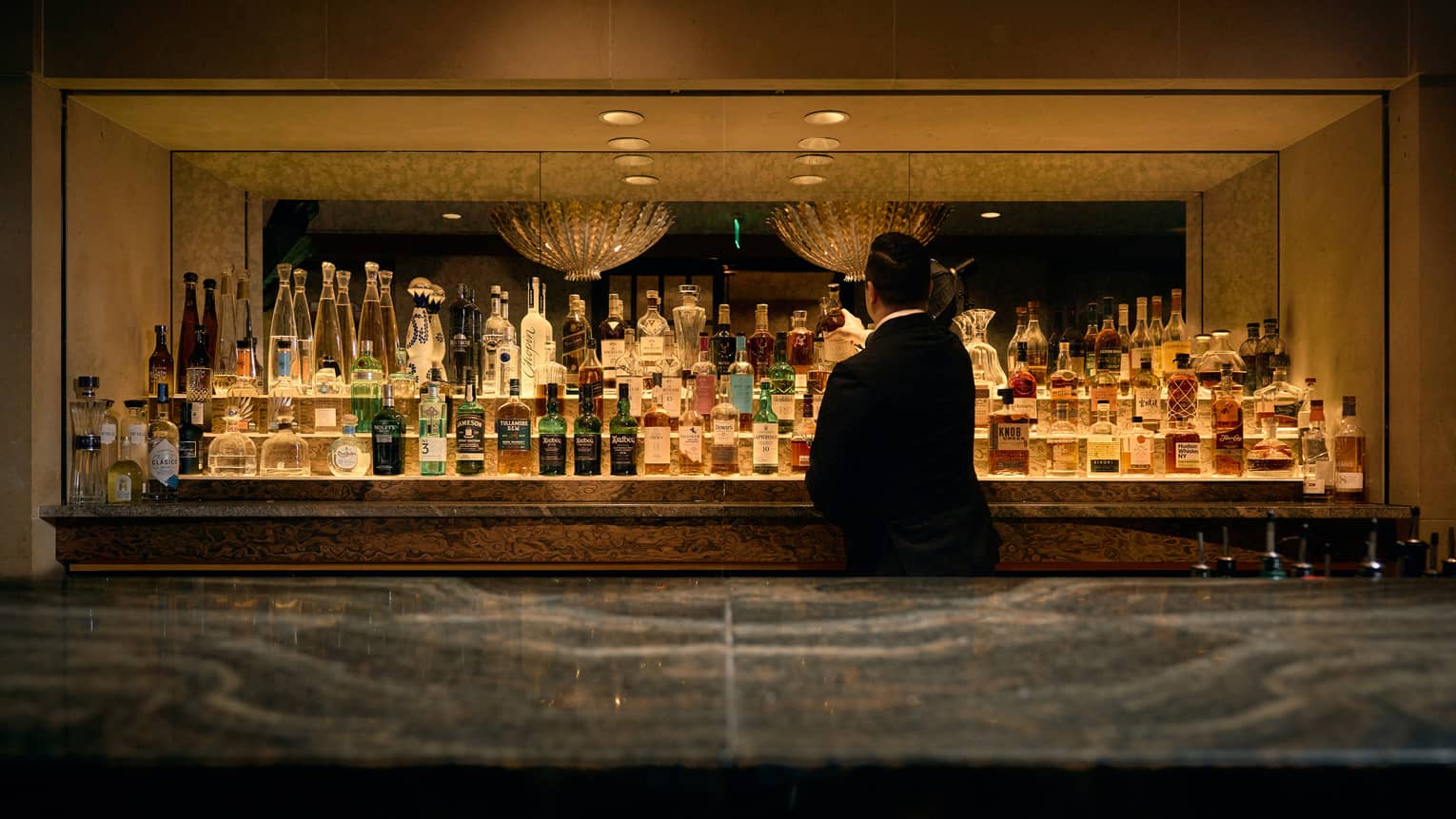 Bartender standing behind the bar near a display of bottles.