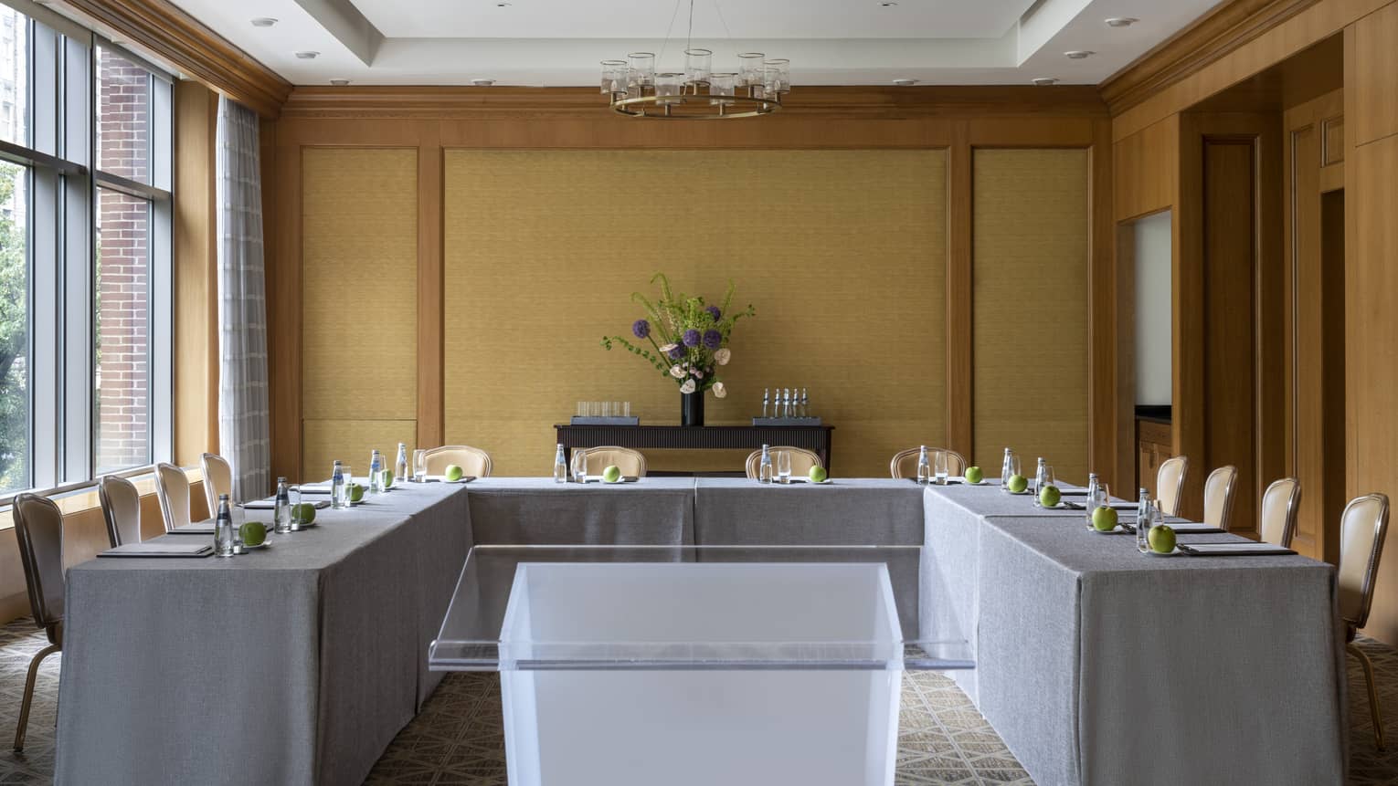 A U-shaped table with grey cloth and a clear podium in the middle.