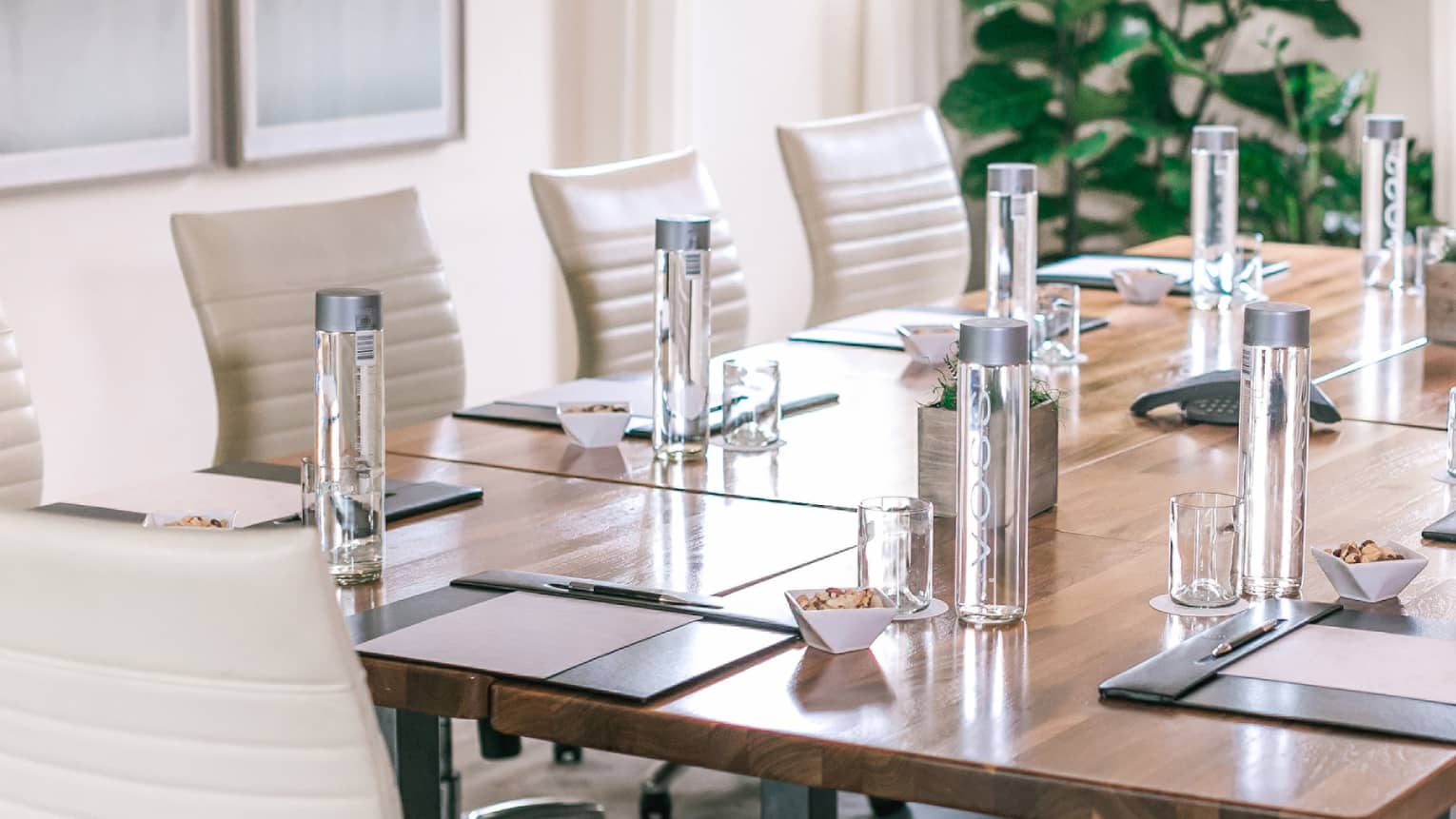 A rectangular boardroom table set with clear glass water bottles and black folders in a naturally-lit room