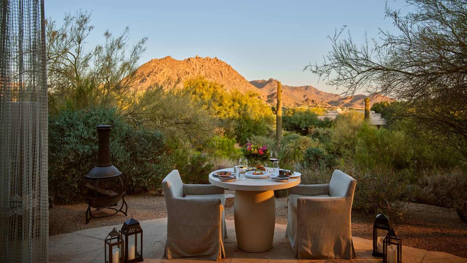Two chairs and a table outside with lanterns and a view of the mountains.