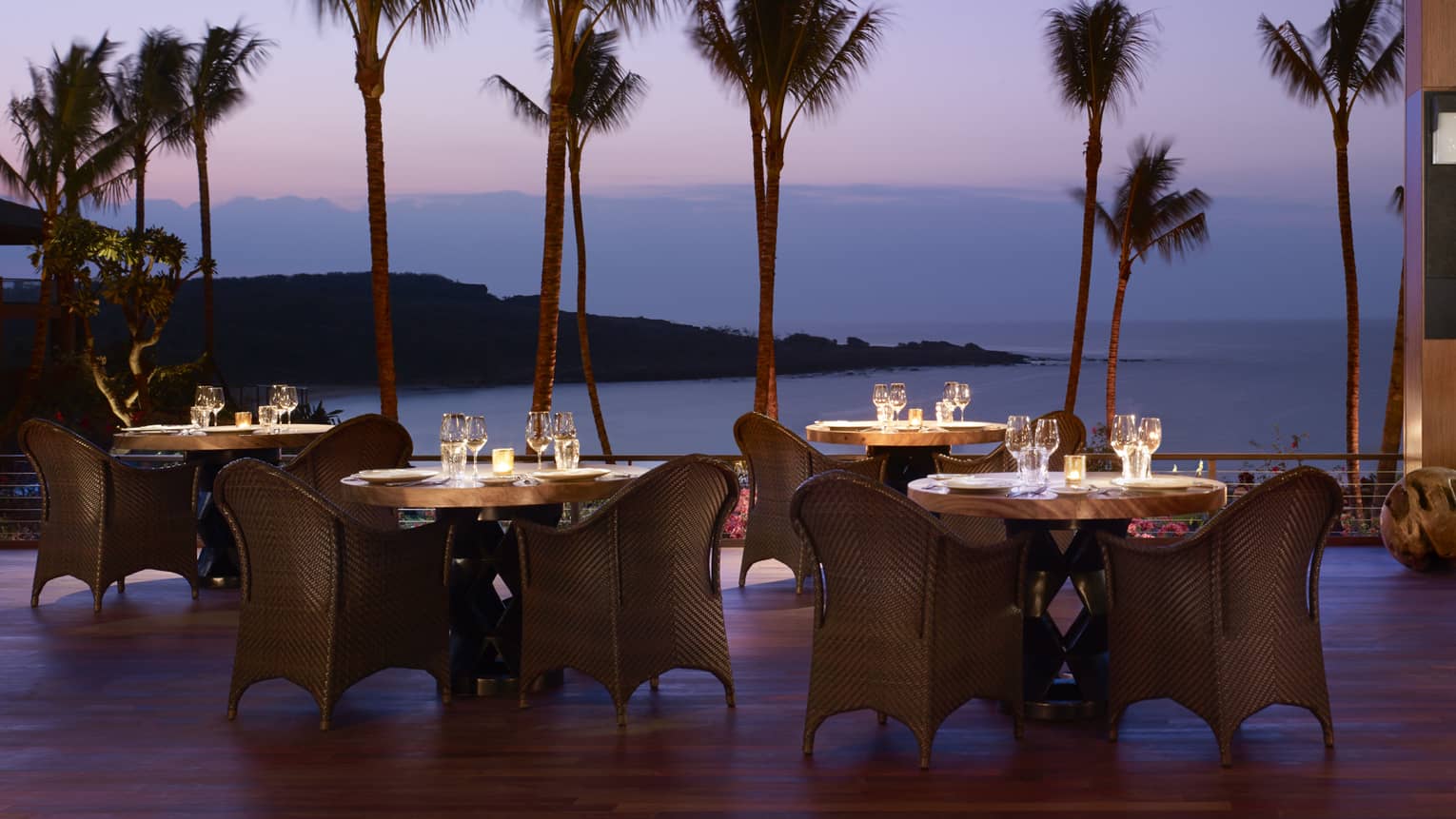 Wicker dining chairs around patio tables overlooking beach on One Forty patio at night