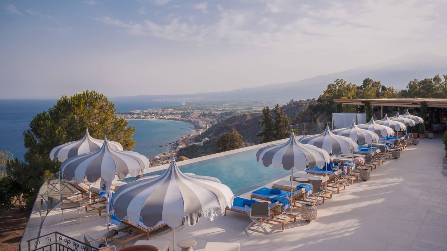 Long rectangular infinity pool with playful striped umbrellas, view of coastline