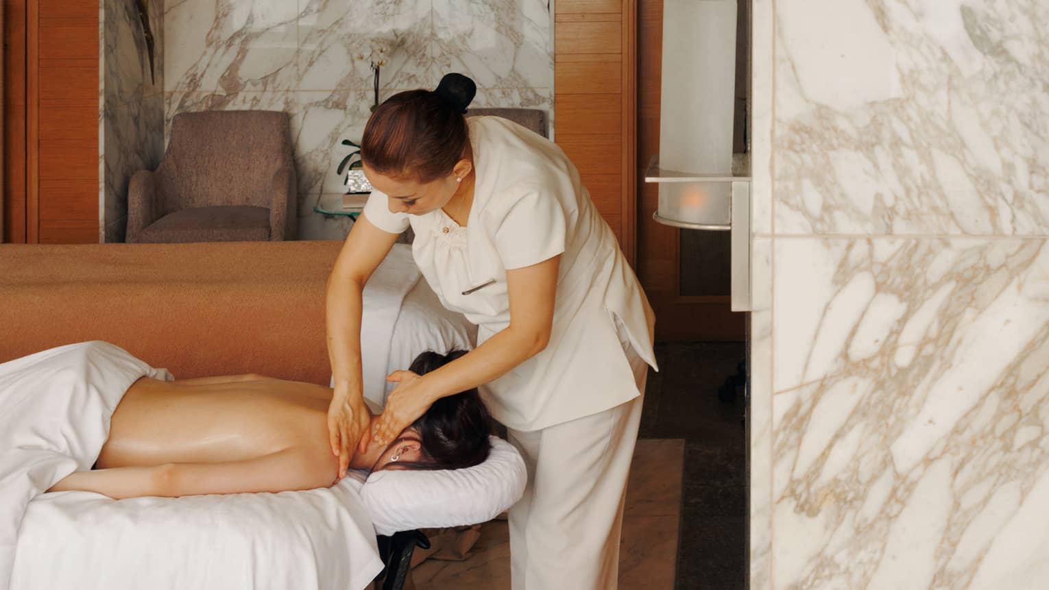 A female spa therapist performing a massage on a woman, face down on spa treatment table, in a chic luxury spa with marble walls