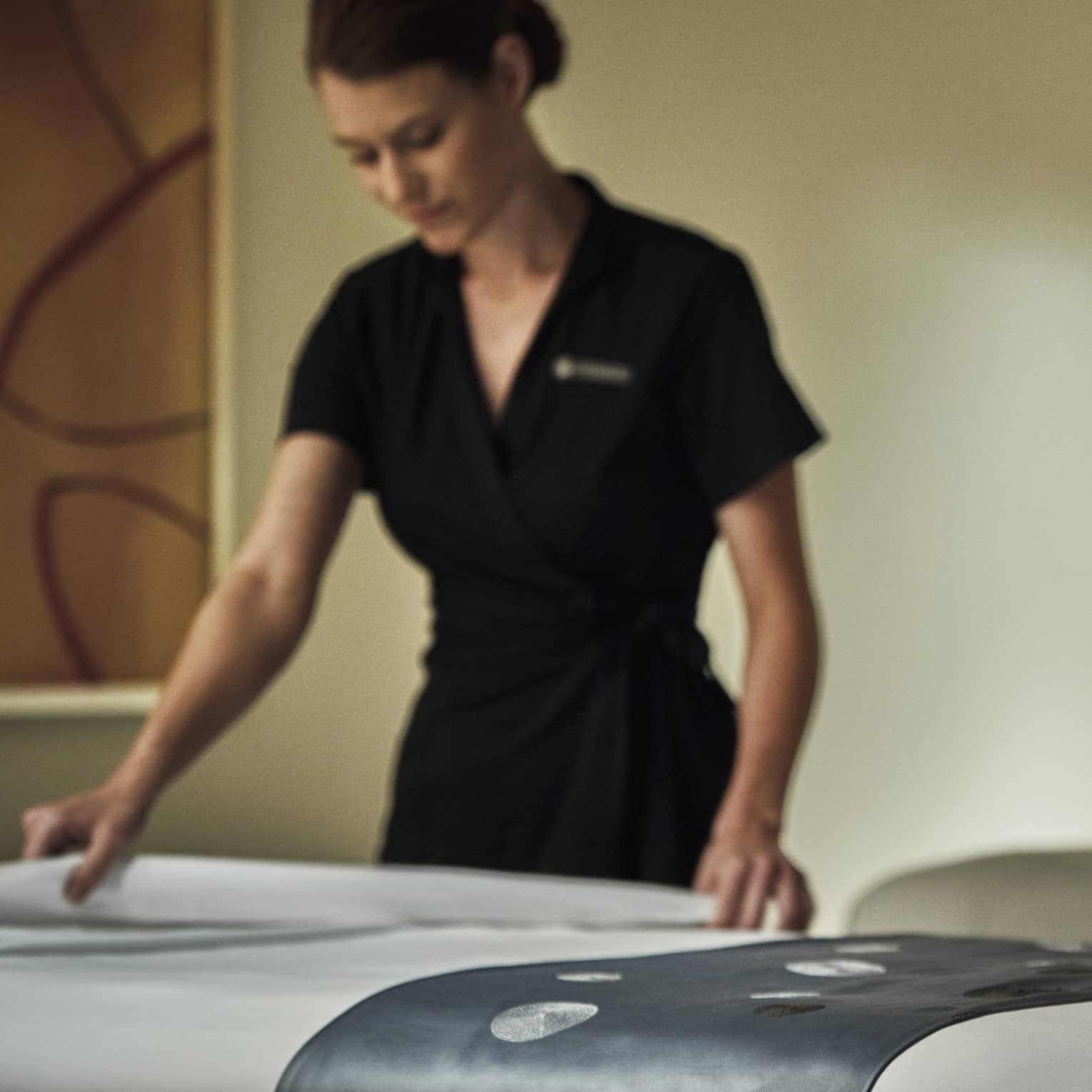 Spa attendant in black dress folds down white sheet on massage table