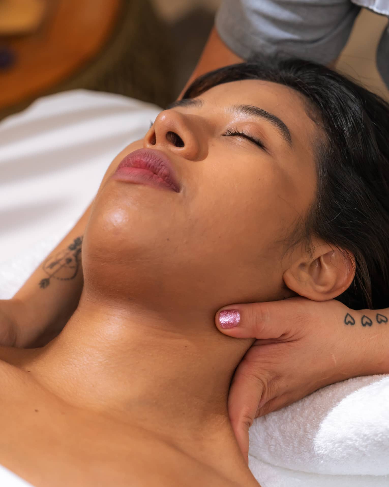 Woman relaxes with eyes closed as massage therapist massages her neck
