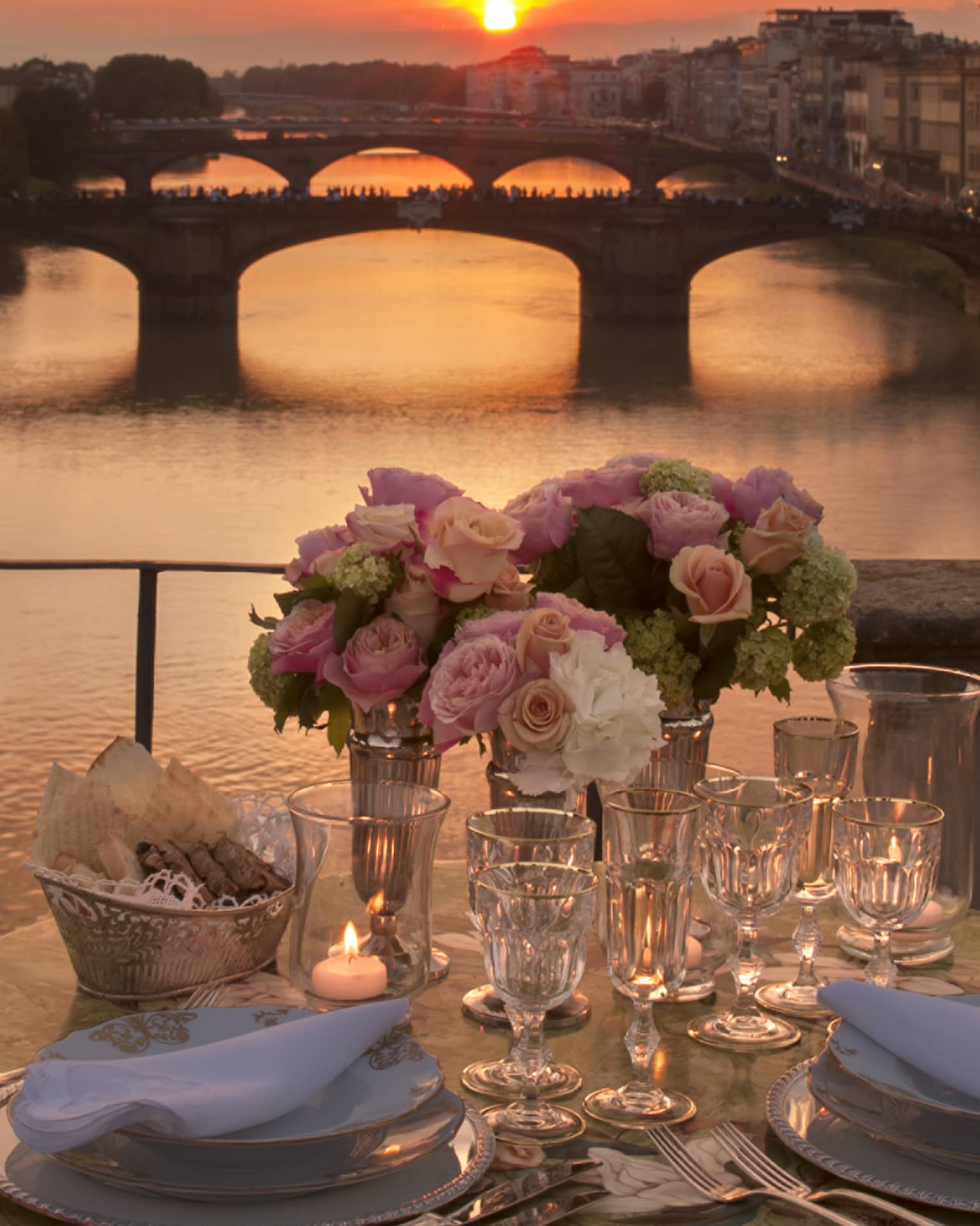 Pink roses in vases on formal dining table on bridge overlooking canal, sunset