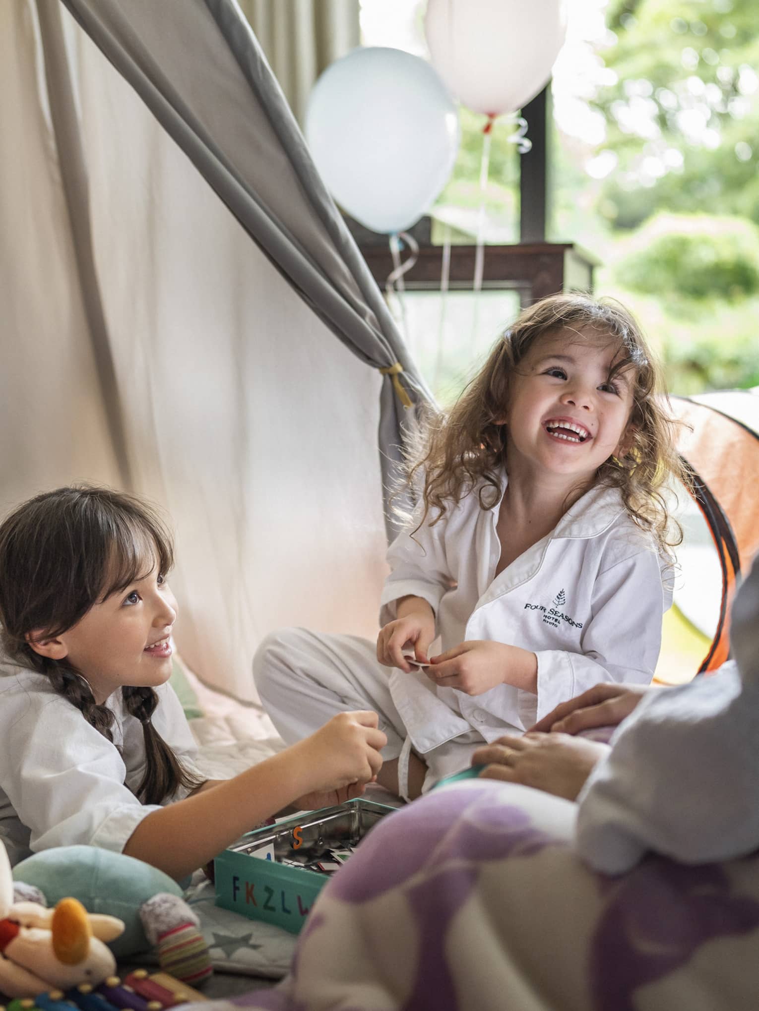 Two children in Four Seasons pajamas, smiling and playing together in a cozy indoor tent setup