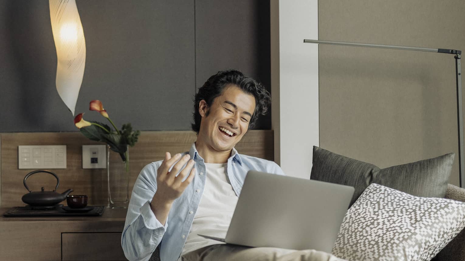 Laughing man lounges on sofa with laptop in his guest room