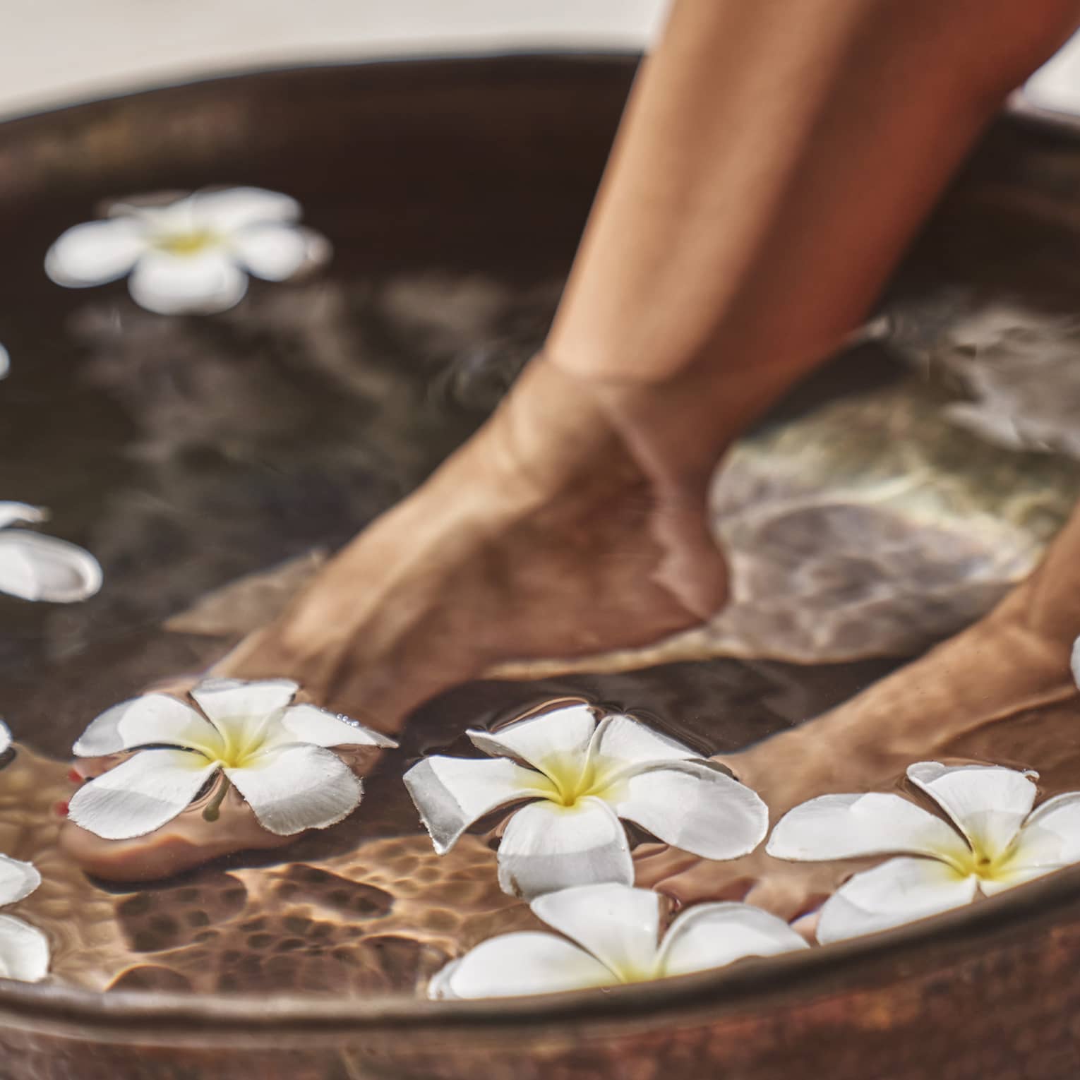 A woman's feet in a bowl of water and flowers.
