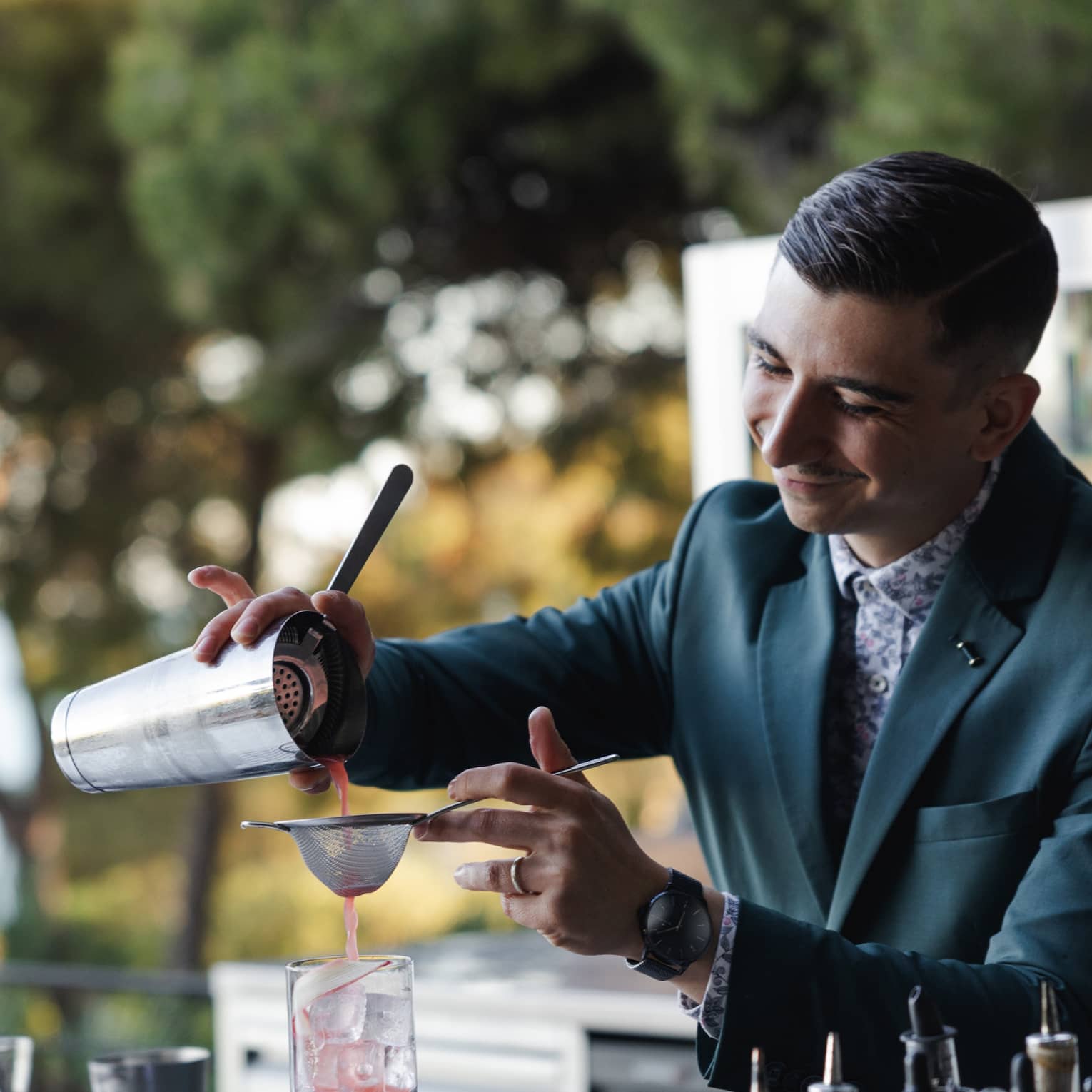 A bartender pours a pink beverage through a strainer into a glass with ice