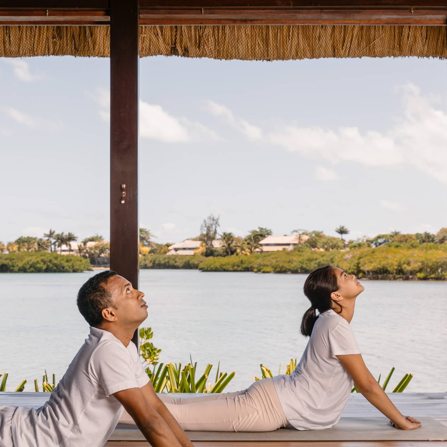Two people practising yoga in an open to outside area.