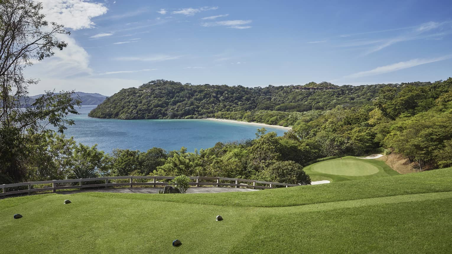 Green golf course driving range lawn and path on hills overlooking ocean