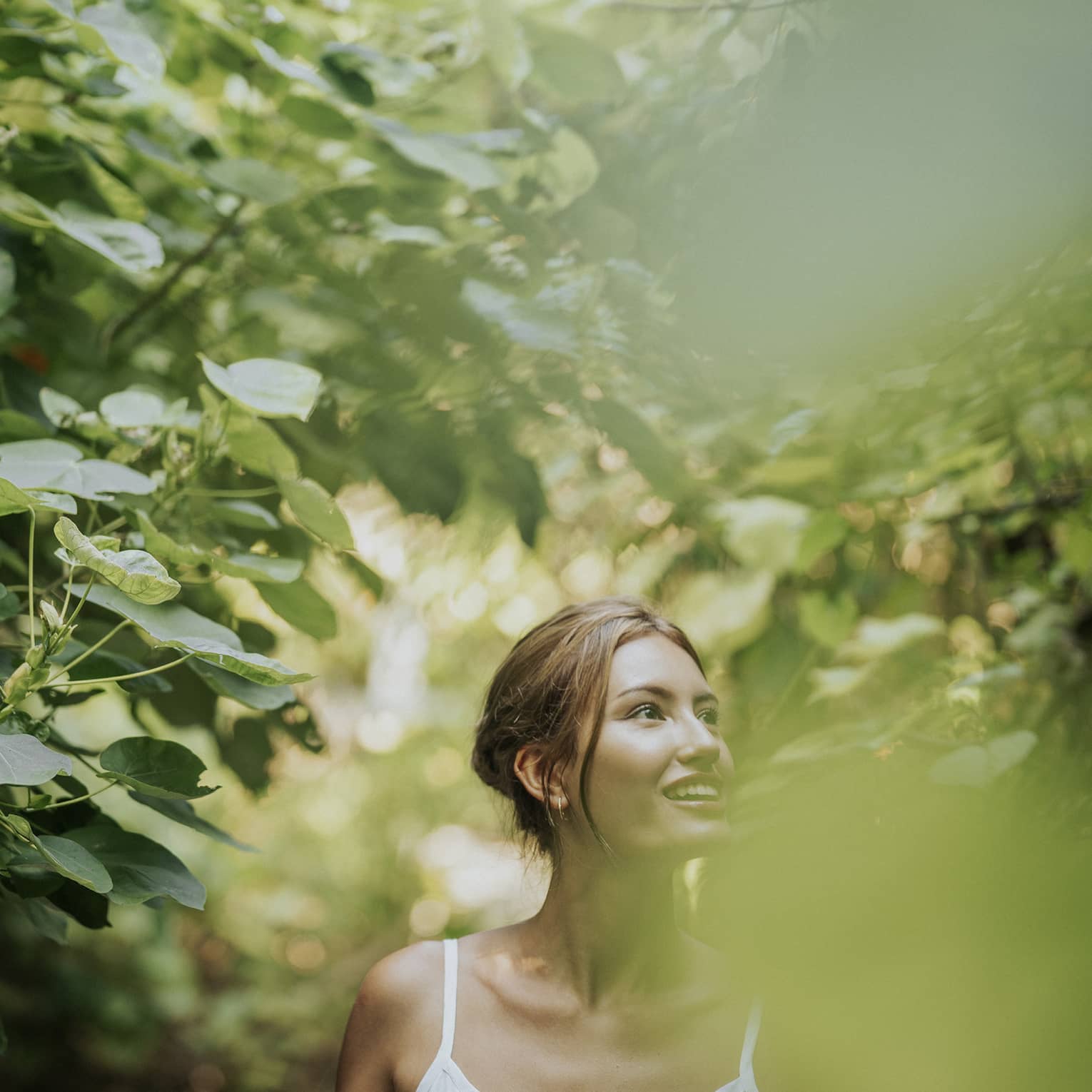Woman in white tank top walks along heavily tree-lined path