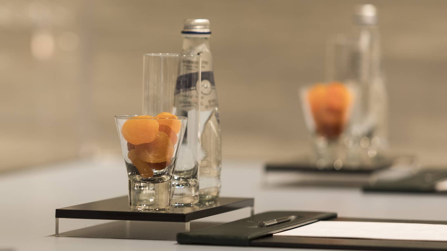 Close-up of meeting table place setting with agenda, dried apricots in glass, bottle of sparkling water