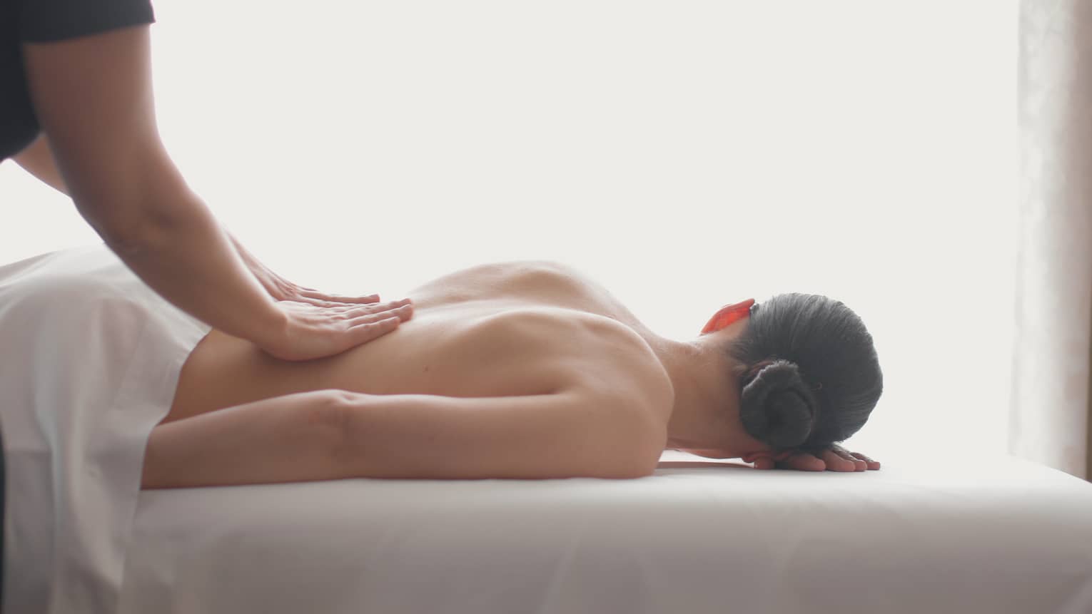Side view of woman lying on massage table, hands massaging her bare shoulders