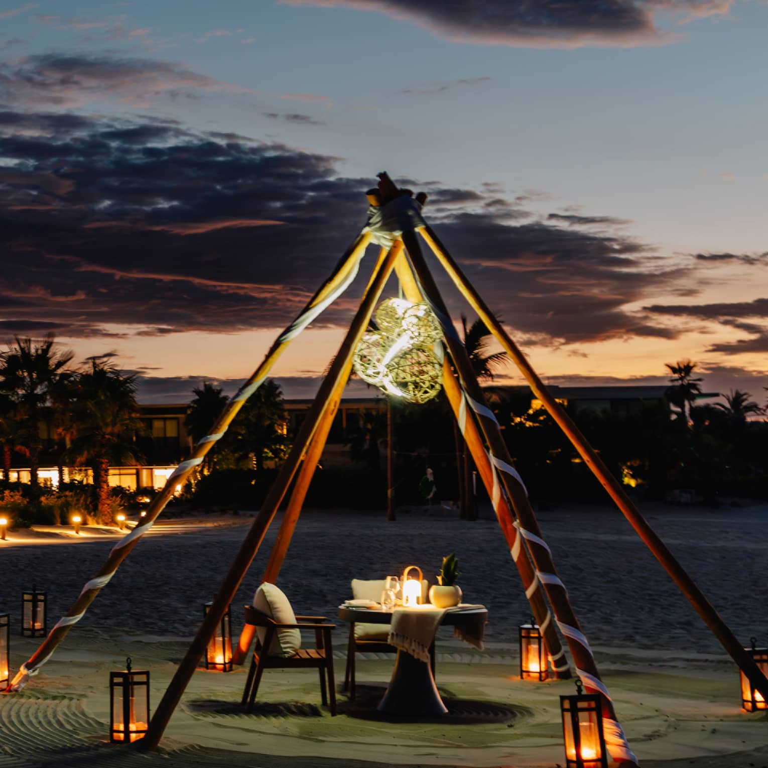 Outdoor tent with a chair and dining table, surrounded by lanterns on the ground in the evening.