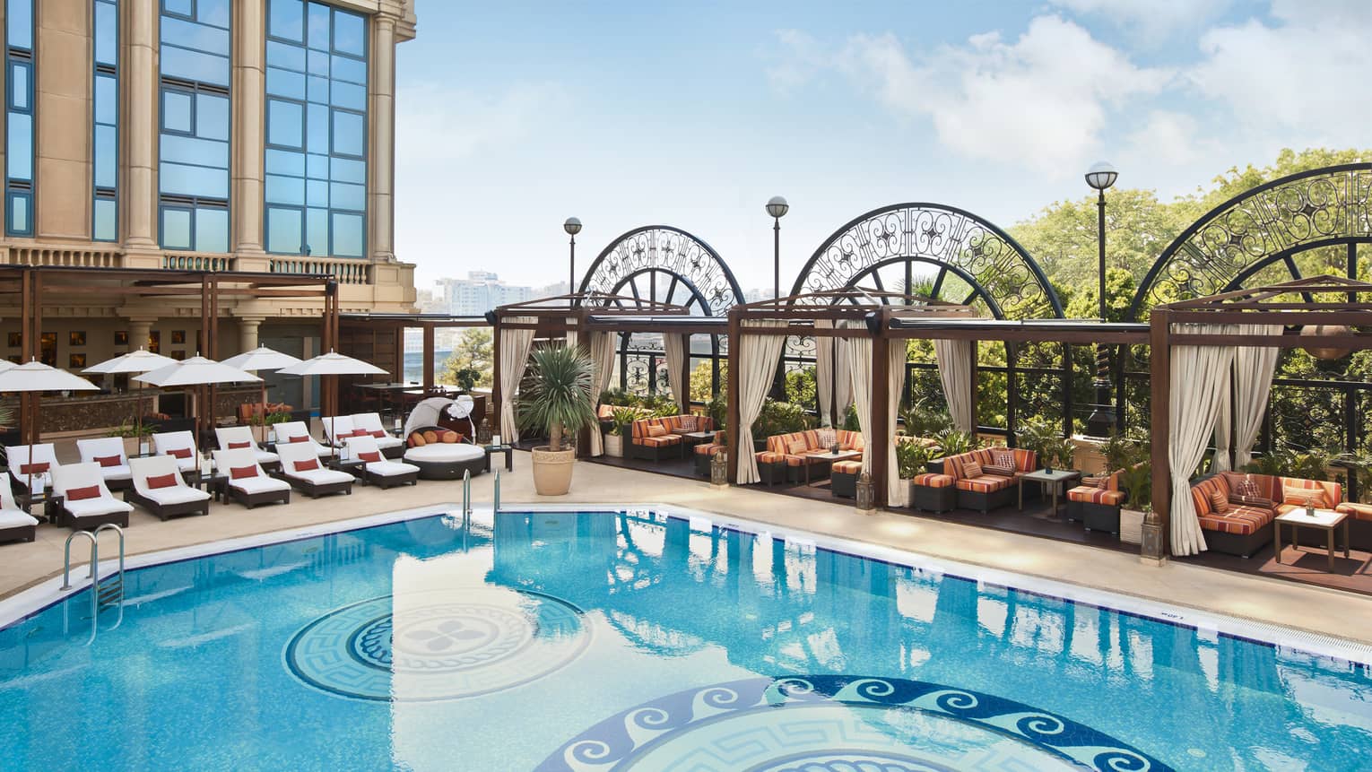Looking down at sunny fourth-floor patio and outdoor swimming pool lined with lounge chairs, cabanas