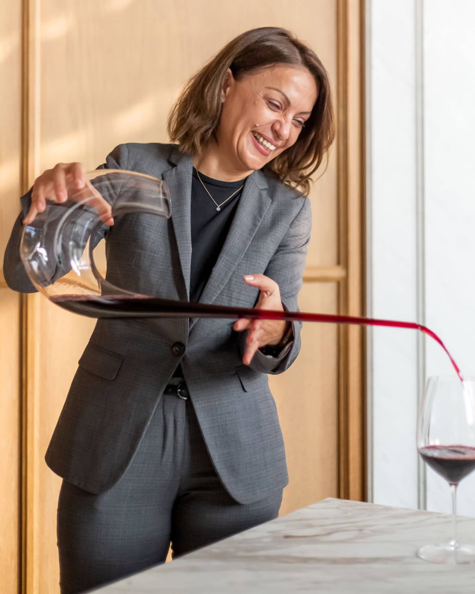 Brasserie Palmier Bar sommelier smiles, pours red wine from long decanter into wine glass on table
