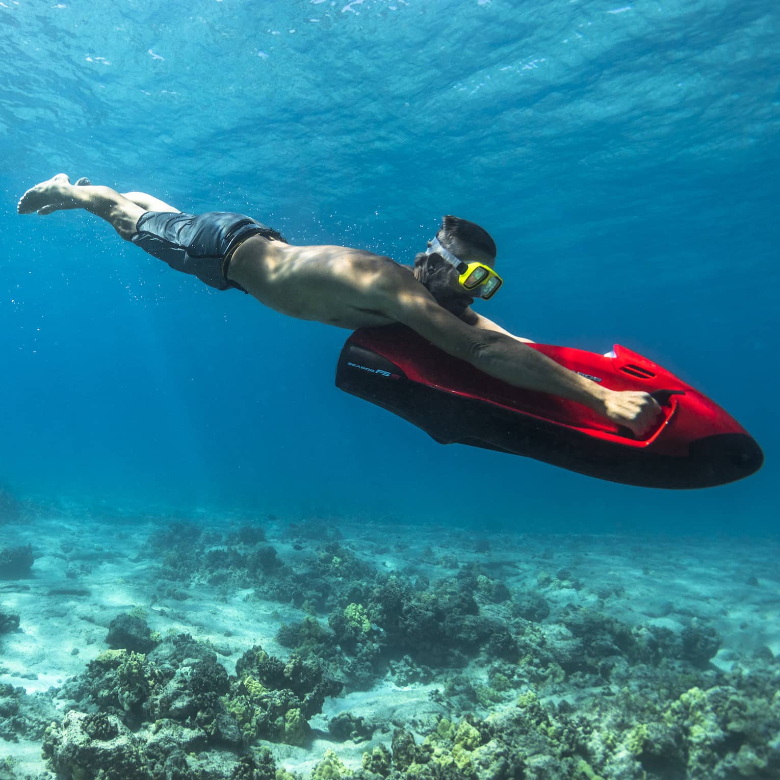 Man dives in ocean over coral, holding red inflatable board