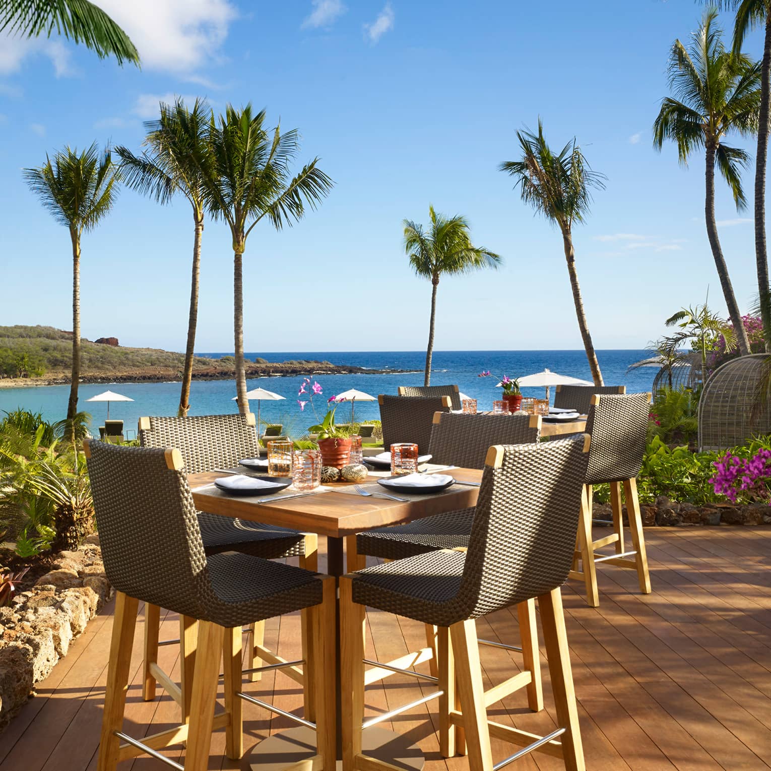 Malibu Farm Bar dining table, chairs on sunny patio overlooking beach, ocean