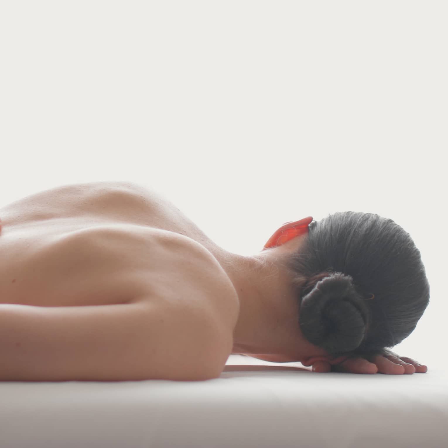 Side view of woman lying on massage table, hands massaging her bare shoulders