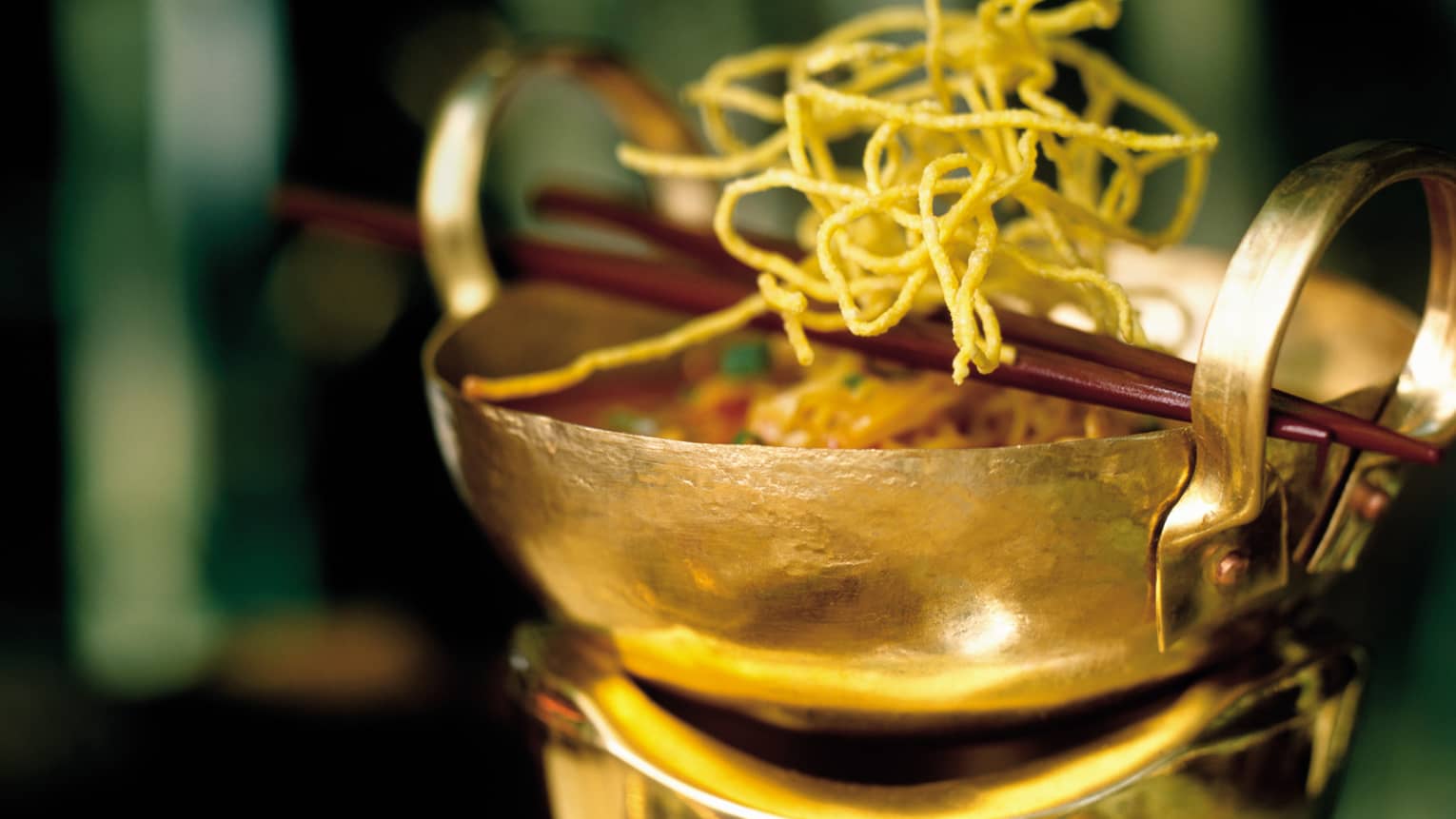 Tom Saab Gai Laotian chicken soup in gold bowl topped with fried noodles, chopsticks